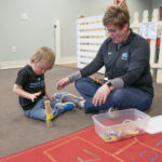 A Physical Therapist at Kinetic Edge Physical Therapy Center works with an infant on crossing midline tasks to help progress to crawling