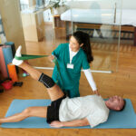 A physical therapist helps a patient to manage chronic pain by stretching injured leg with resistance band