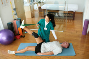 A physical therapist helps a patient to manage chronic pain by stretching injured leg with resistance band