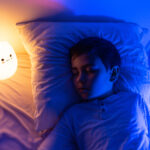 six years old bouy sleep with LED night lamp, School child dreaming. Kid angry of darkness.