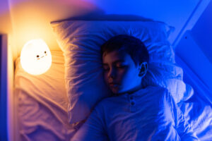 six years old bouy sleep with LED night lamp, School child dreaming. Kid angry of darkness.