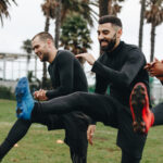 Cheerful football players doing warm up exercises on the field before the match. Happy footballers doing leg raises standing on the field.