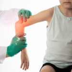 The hands of a traumatologist doctor in green medical gloves examine the girl s damaged elbow joint. Injury and dislocation of the elbow joint, bruise and fracture. Growing pains