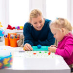 Toddler girl in child occupational therapy session doing sensory playful exercises with her therapist.